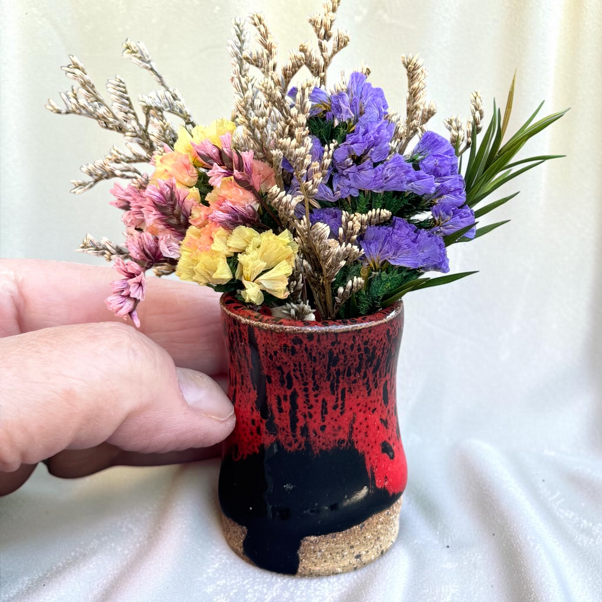 Rock N Art Shop mini ceramic bud vase with red and black glaze and dried flowers held in a hand