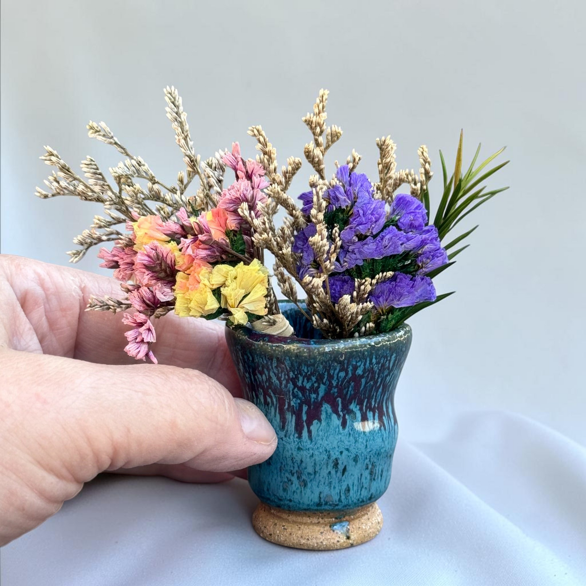 Rock N Art Shop miniature ceramic bud vase with turquoise and plum glaze, held in hand with dried colorful flowers.