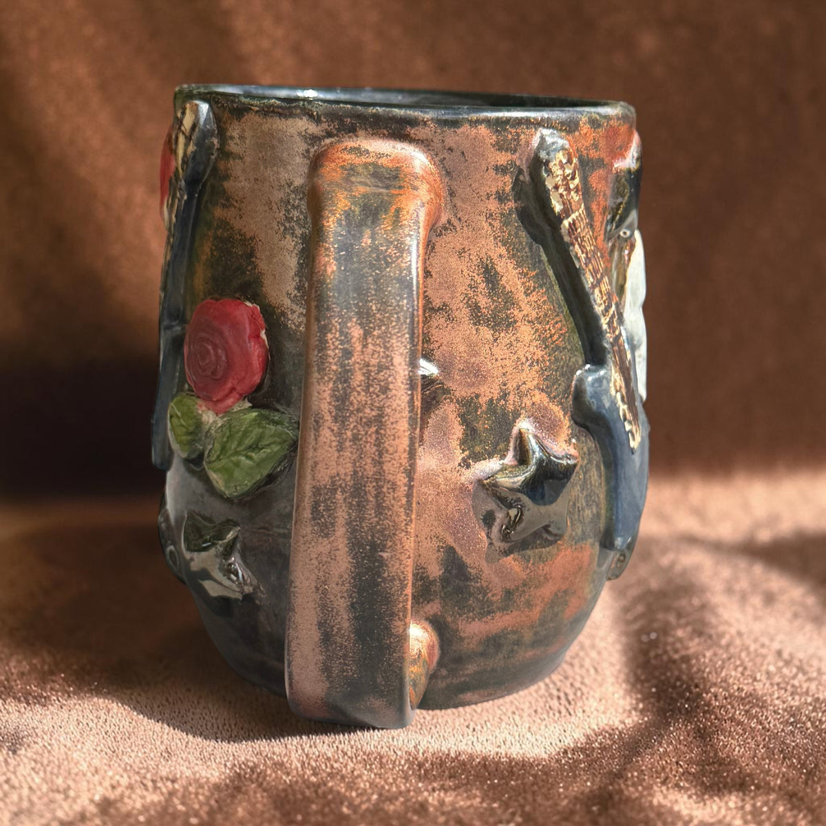 Rock N Art Shop handmade stoneware mug with bronze glaze, sculpted skull, guitar, red rose, and star details.