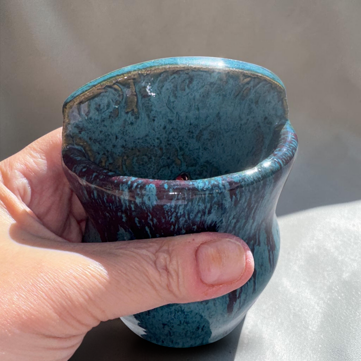 Rock N Art Shop turquoise and blue stoneware wall pocket vase with plum-brown glaze drips held in a hand.