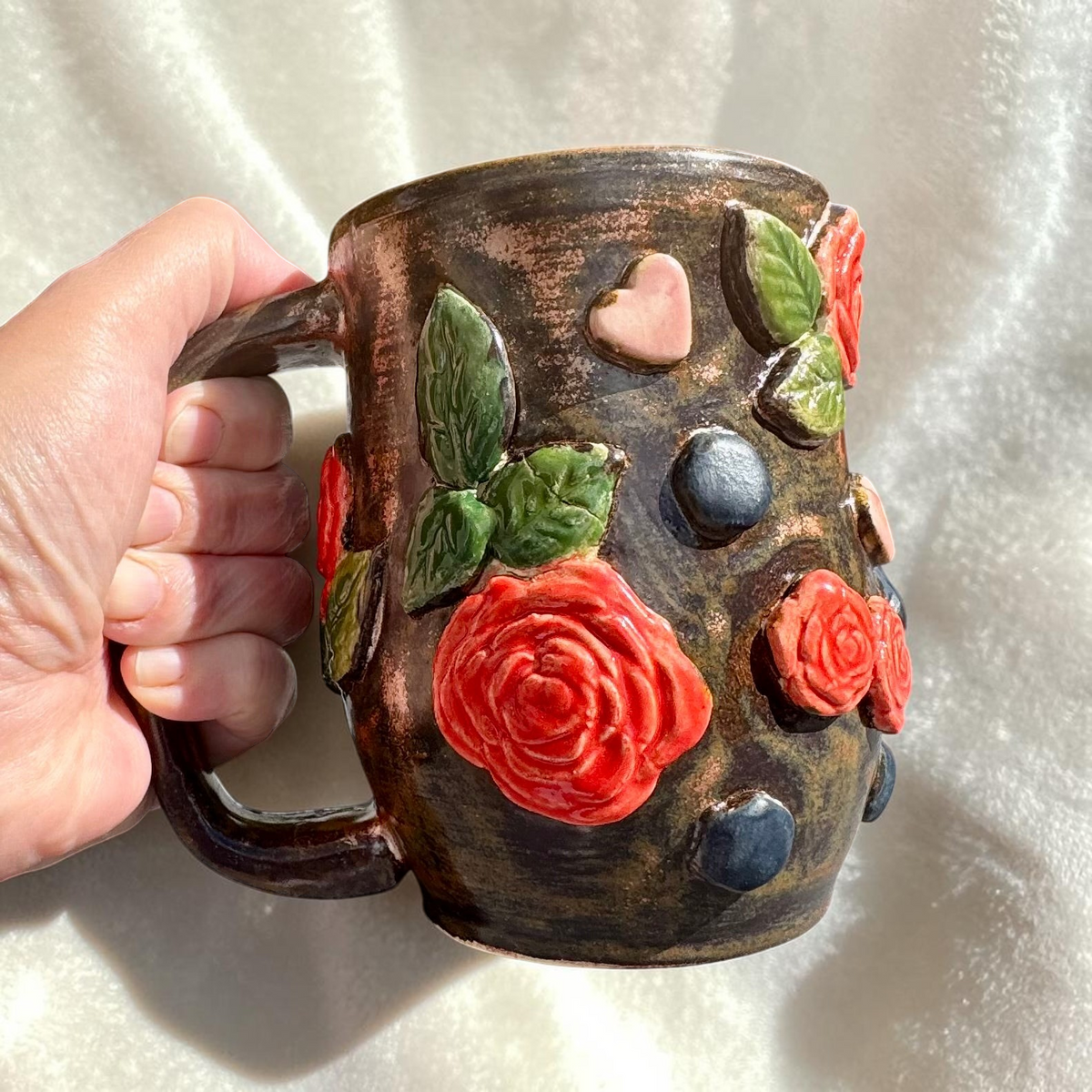 Rock N Art Shop handmade stoneware mug with dimensional red roses, green leaves, and pink hearts on a bronze glaze.