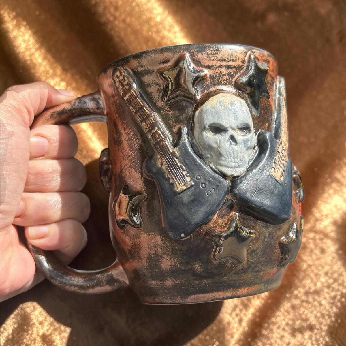Rock N Art Shop handmade 16 oz stoneware mug with sculpted skull, electric guitar, and star details in bronze glaze.