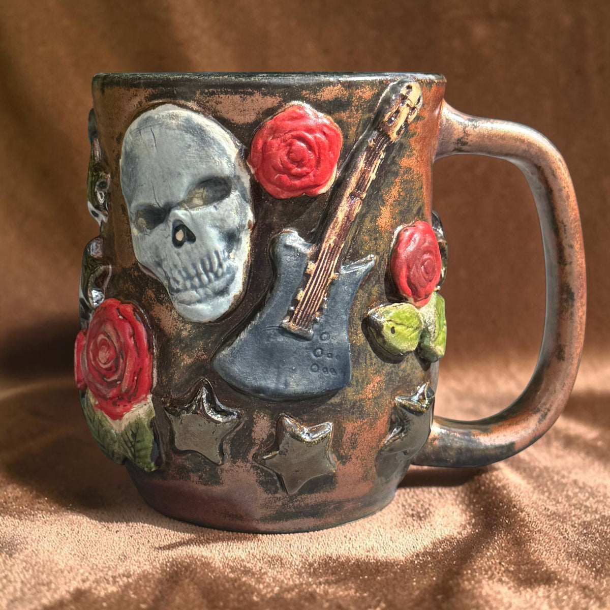 Rock N Art Shop handmade stoneware mug featuring sculpted skulls, electric guitars, and red roses in bronze glaze.