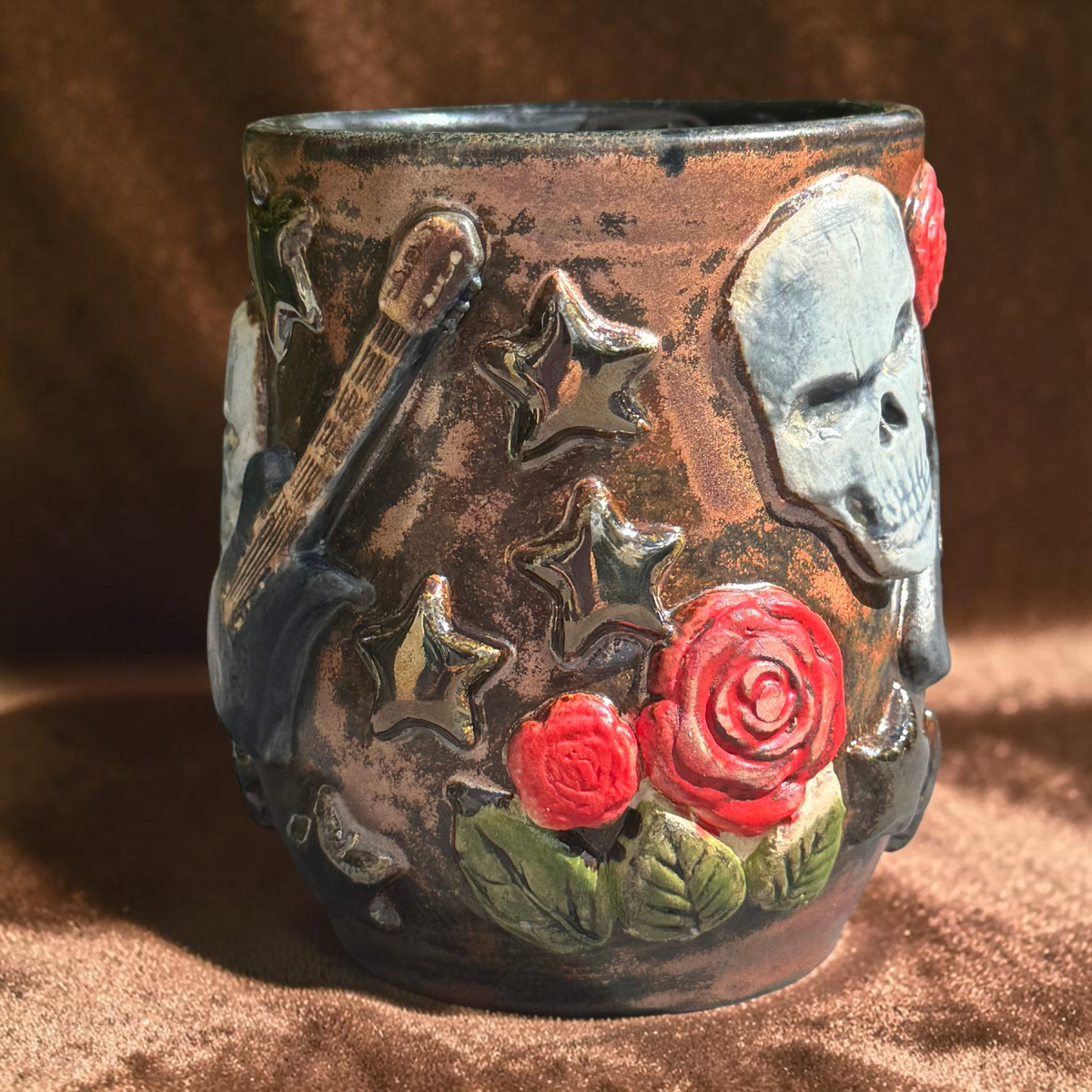 Rock N Art Shop handmade 16 oz stoneware mug featuring sculpted skulls, guitars, red roses, and bronze metallic stars.