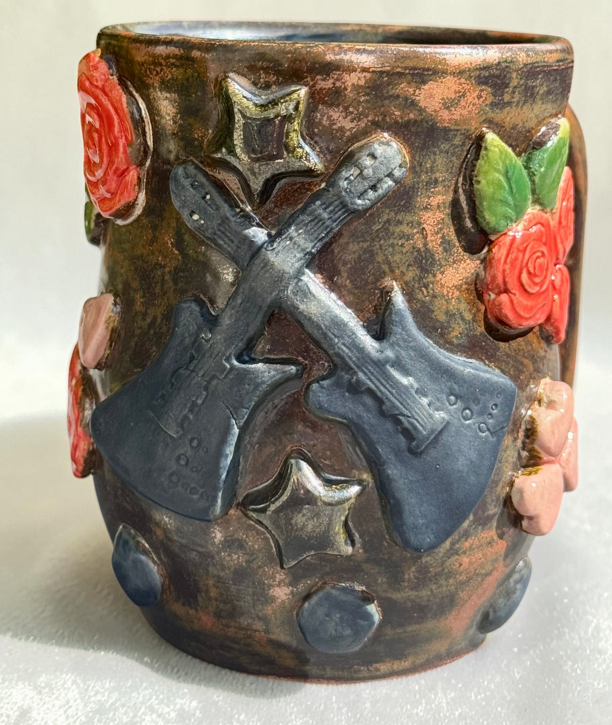 Rock N Art Shop handmade stoneware mug featuring crossed electric guitars, red roses, and metallic stars on bronze glaze