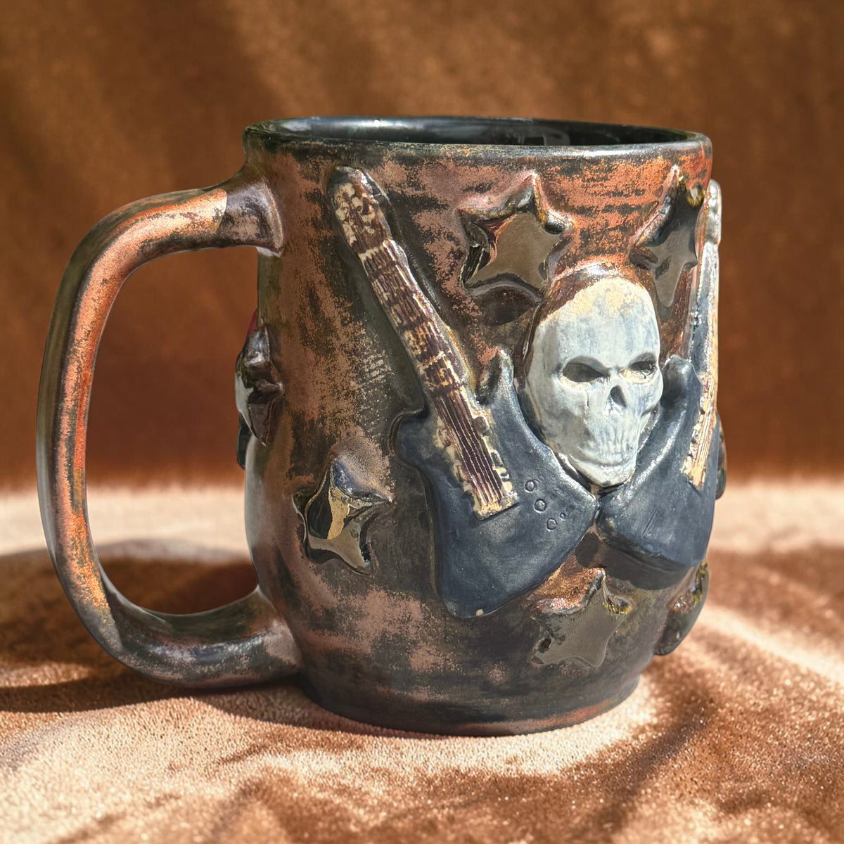 Rock N Art Shop 16 oz handmade stoneware mug with sculpted skull, electric guitar, and star details in bronze glaze.