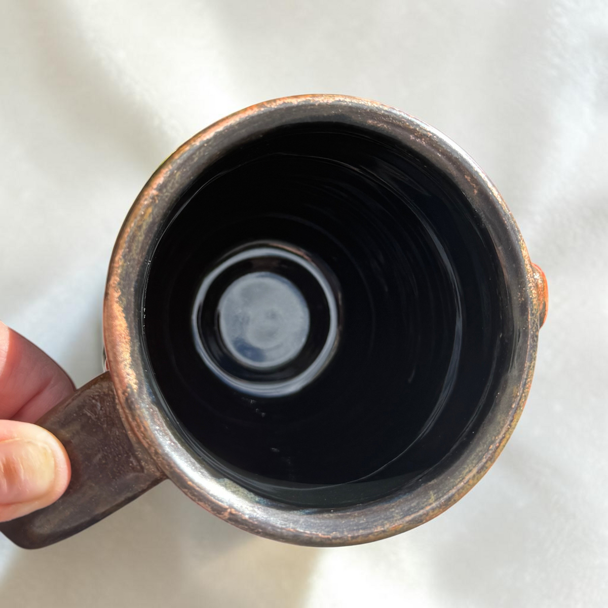 Top-down view of a Rock N Art Shop 16 oz handmade stoneware mug with a glossy dark interior and bronze-toned rim.