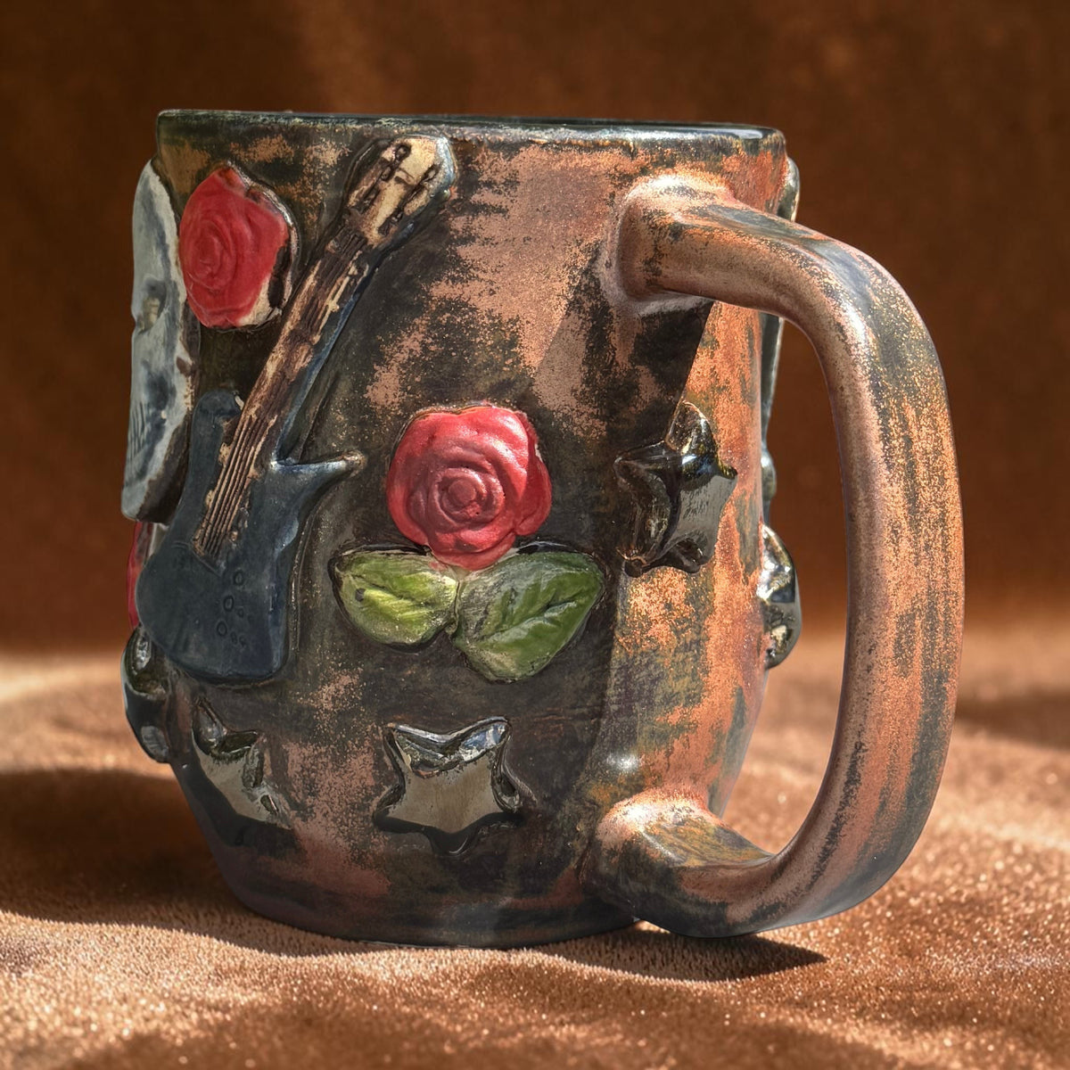 Rock N Art Shop handmade stoneware mug featuring sculpted skulls, electric guitars, and red roses in bronze glaze.