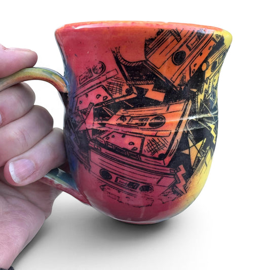 Rock N Art Shop handmade 12 oz ceramic mug with a bold, abstract cassette tape design in red, orange, and yellow.