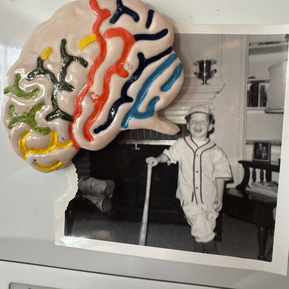 Rock N Art Shop handmade ceramic brain magnet with colorful hand-glazed details holding a vintage photo on a fridge.