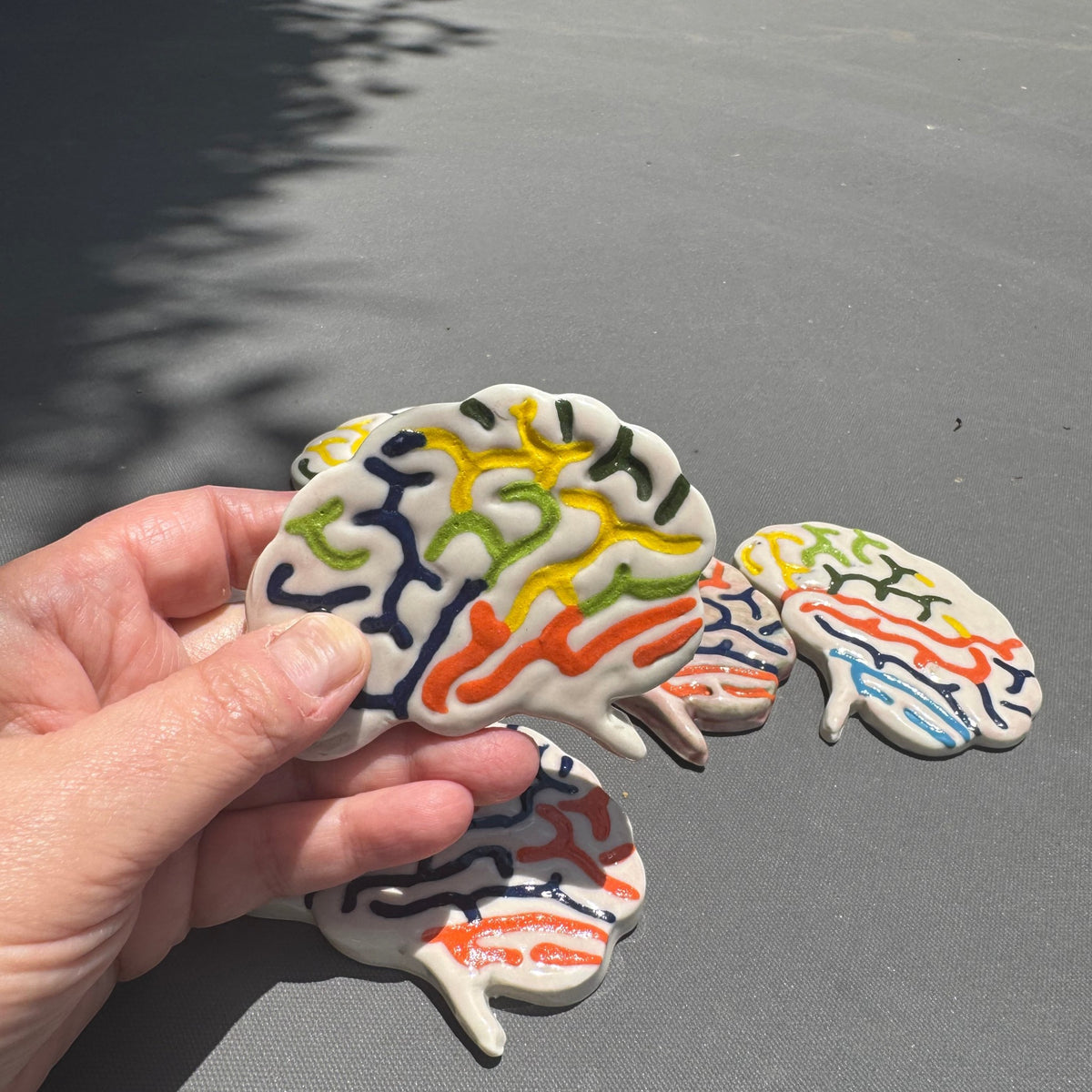 Rock N Art Shop handmade ceramic brain magnet with colorful hand-glazed anatomical details held in a hand