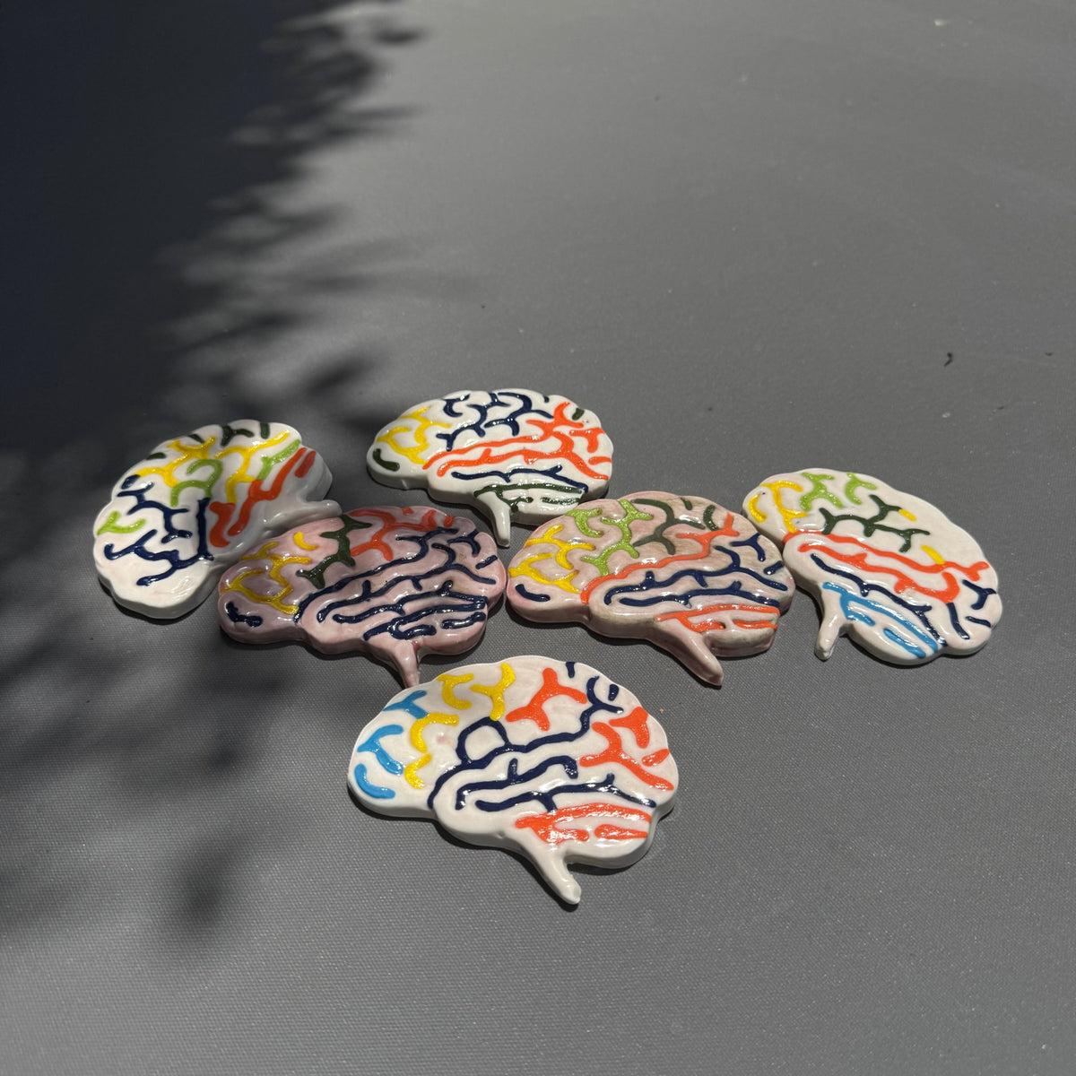 Rock N Art Shop handmade stoneware ceramic brain magnets with colorful hand-glazed anatomical details on a grey surface.
