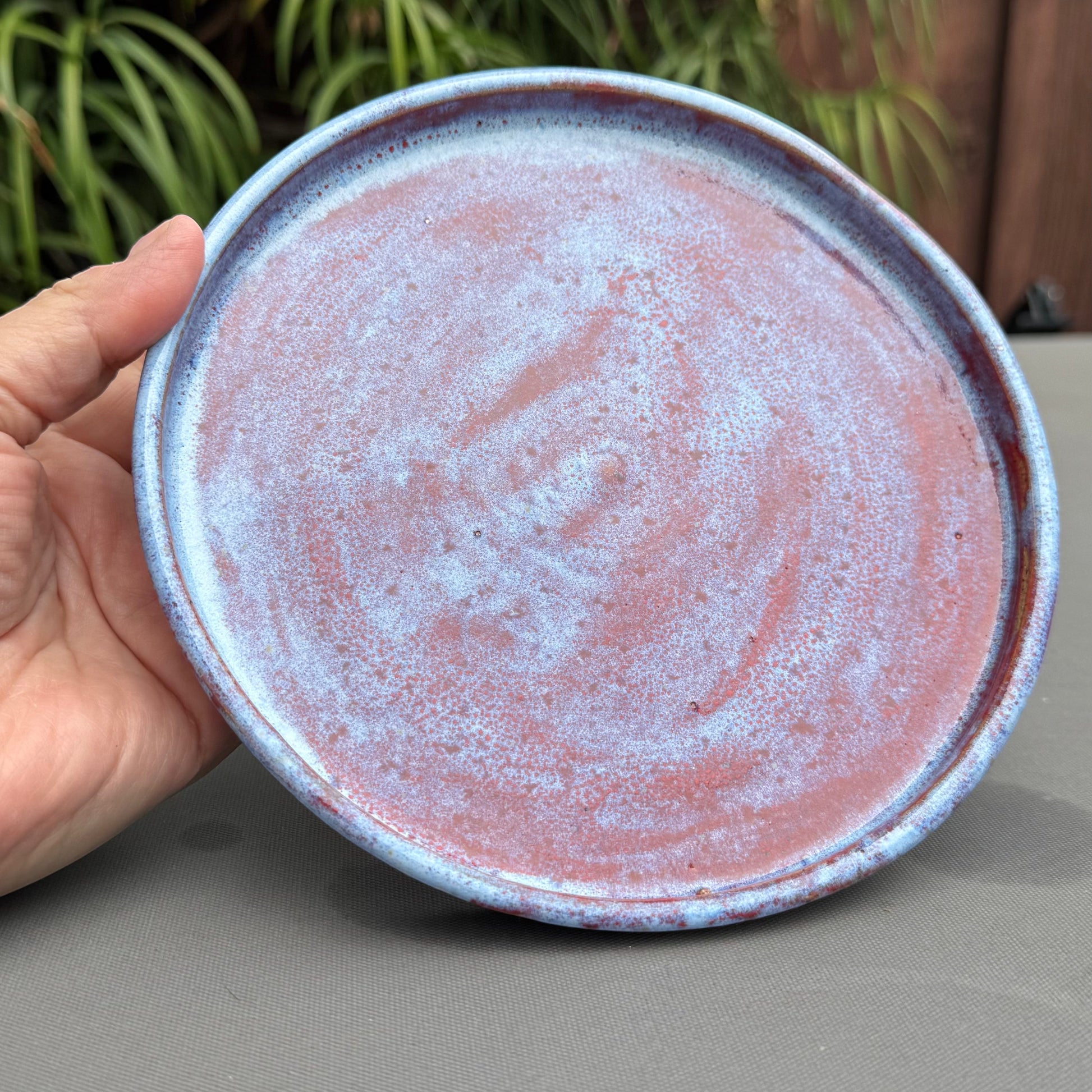 Rock N Art Shop handmade ceramic saucer with a speckled blue and ruby red glaze finish held in a hand.