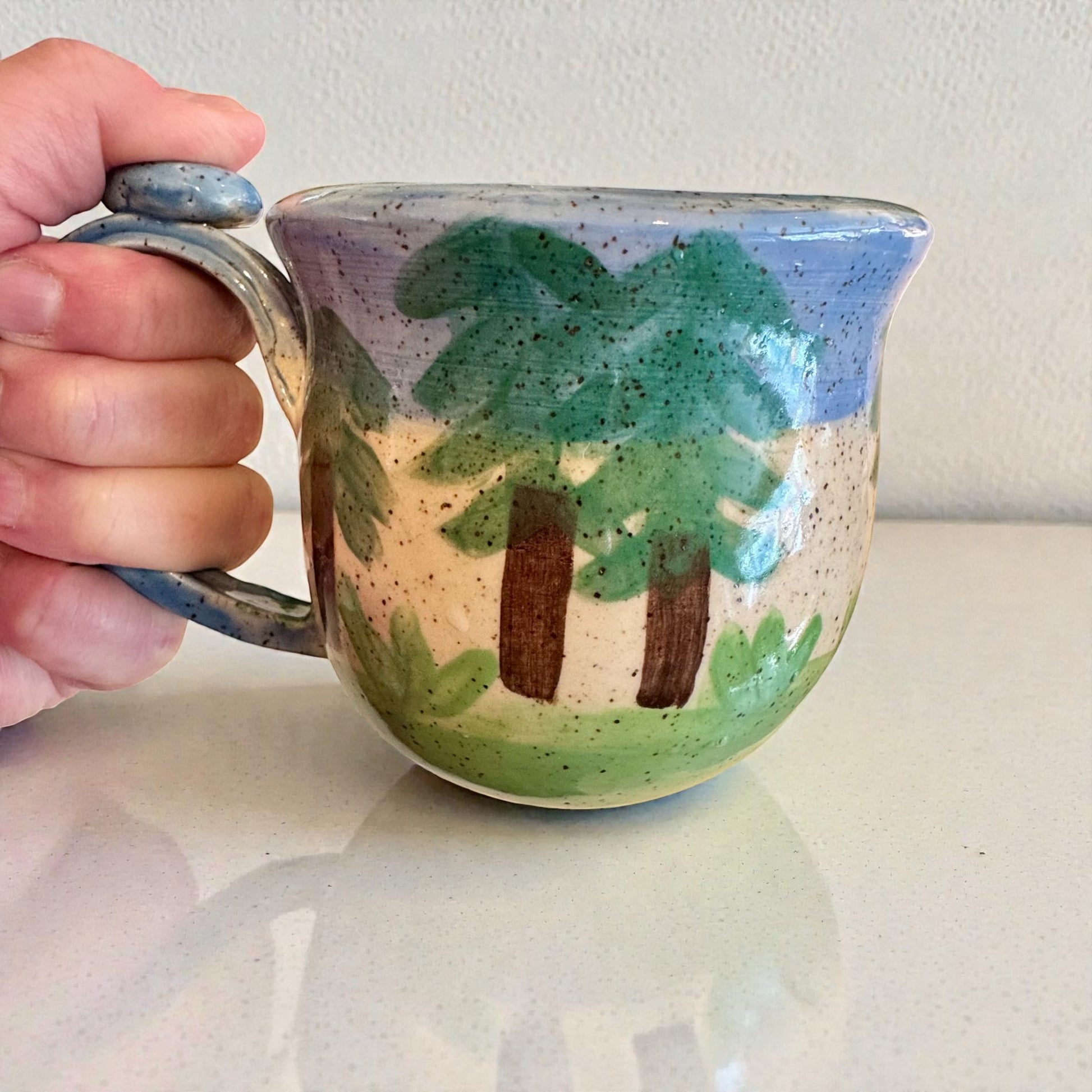 Rock N Art Shop Forest Bear Stoneware Mug with raised bear silhouette and forest scene, hand-glazed in cabin tones of blue, green, and brown. Approx. 12 oz.