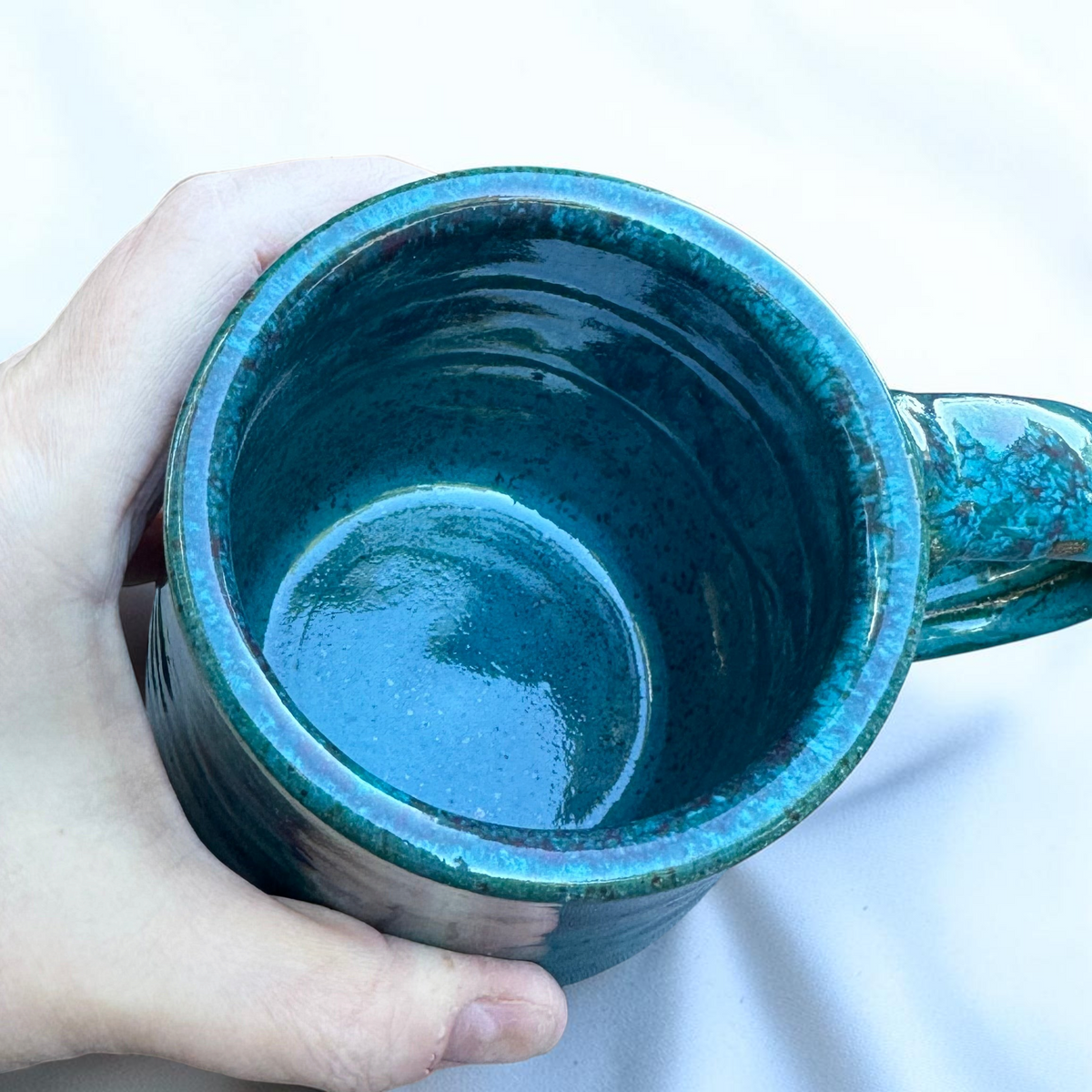 Rock N Art Shop handmade speckled stoneware coffee mug in glossy turquoise blue and purple glaze, top view.