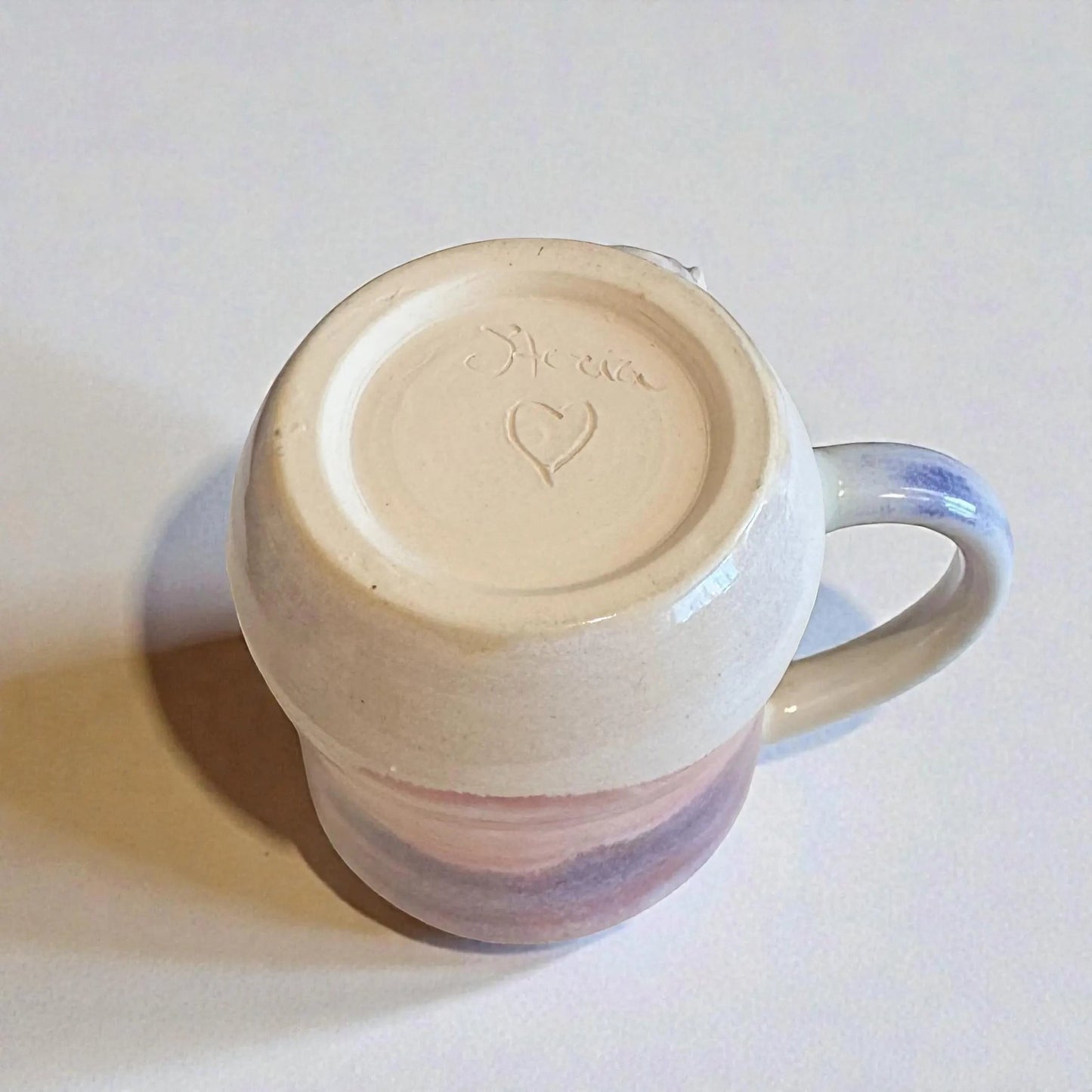 Rock N Art Shop handmade stoneware mug with plum, mauve, and white glaze. Features a heart stamp on the base.
