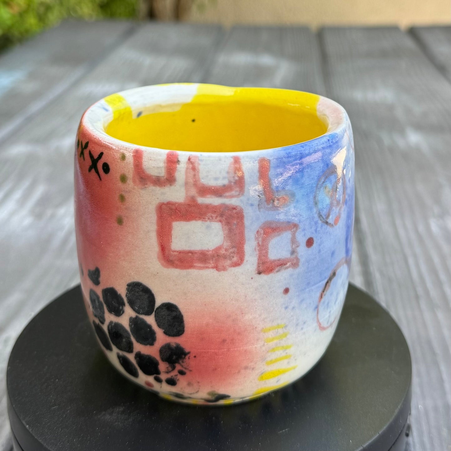 Rock N Art Shop hand-painted stoneware tumbler with abstract pop art design in pink, blue, yellow, and black. Yellow interior.