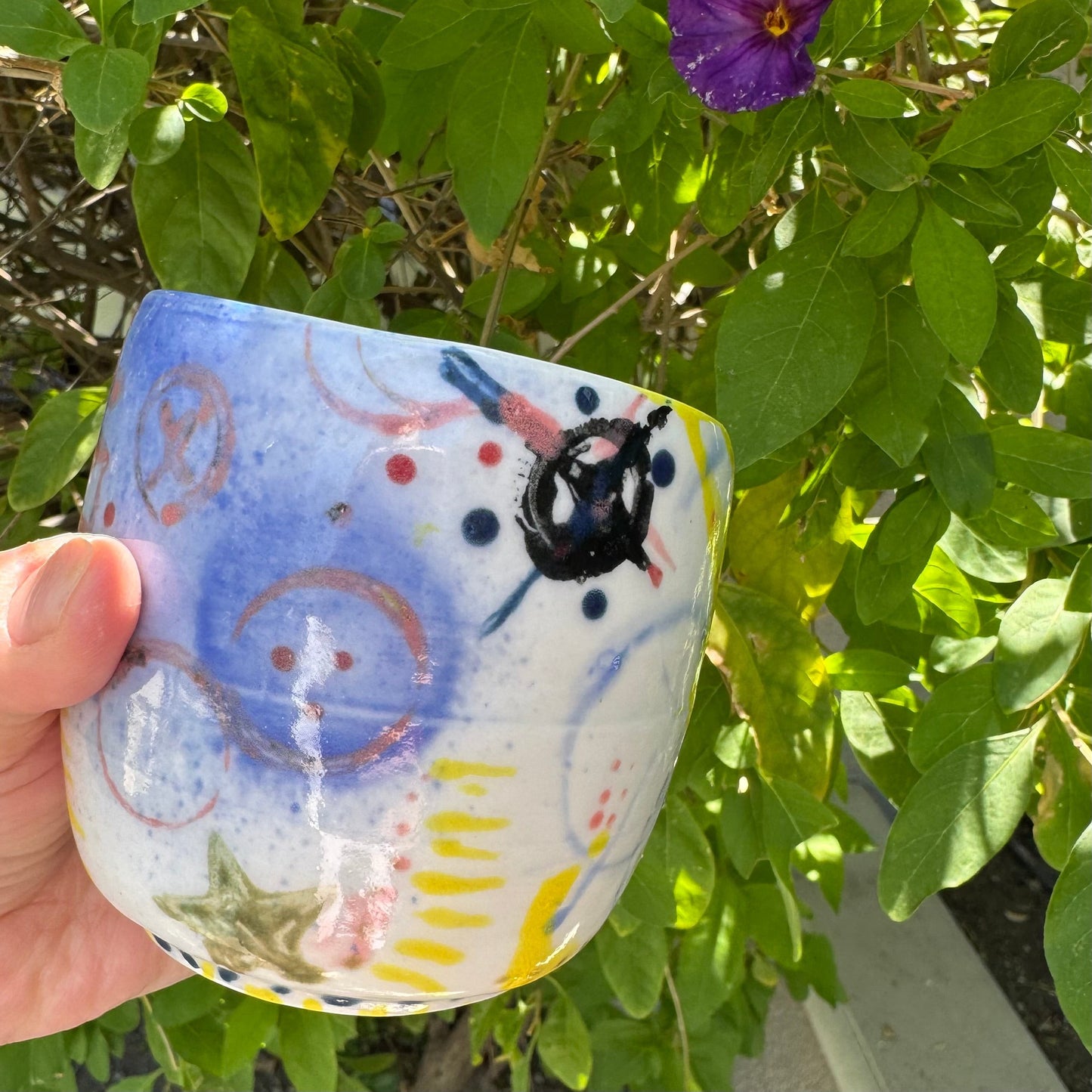 Rock N Art Shop hand-painted stoneware tumbler with abstract pop art design in blue, pink, yellow, and black. 12 oz capacity.