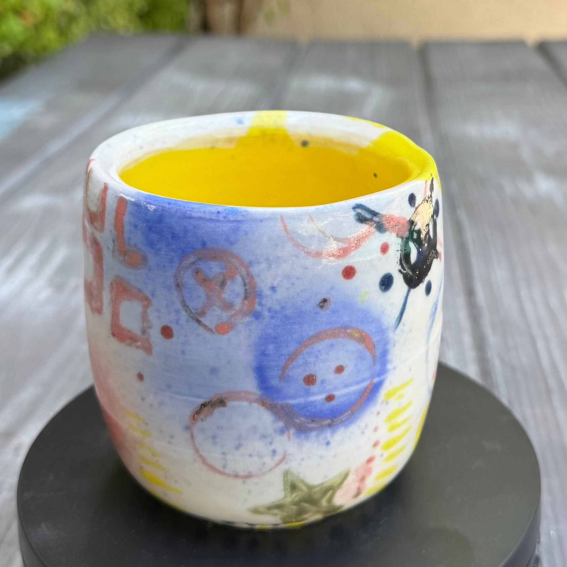 Rock N Art Shop hand-painted stoneware tumbler, 12 oz, with abstract pop art designs in pink, blue, yellow, and black. Bright yellow interior.