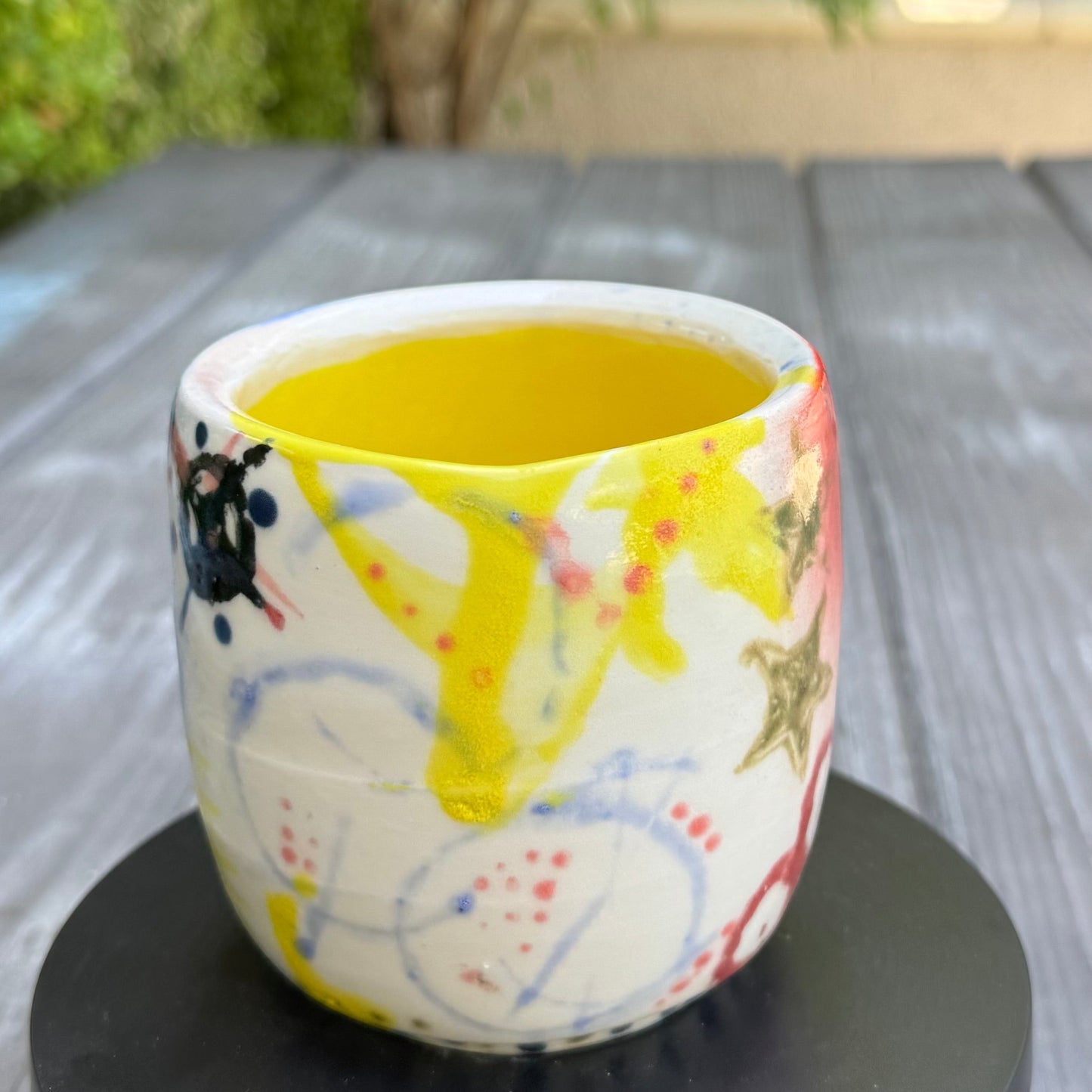 Rock N Art Shop hand-painted stoneware tumbler, 12 oz, with abstract pop art design in pink, blue, yellow, and black, and a bright yellow interior.