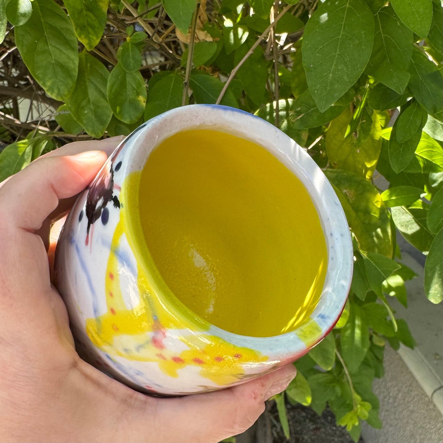 Rock N Art Shop hand-painted stoneware tumbler with pop art design in pink, blue, yellow, and black. Bright yellow interior.