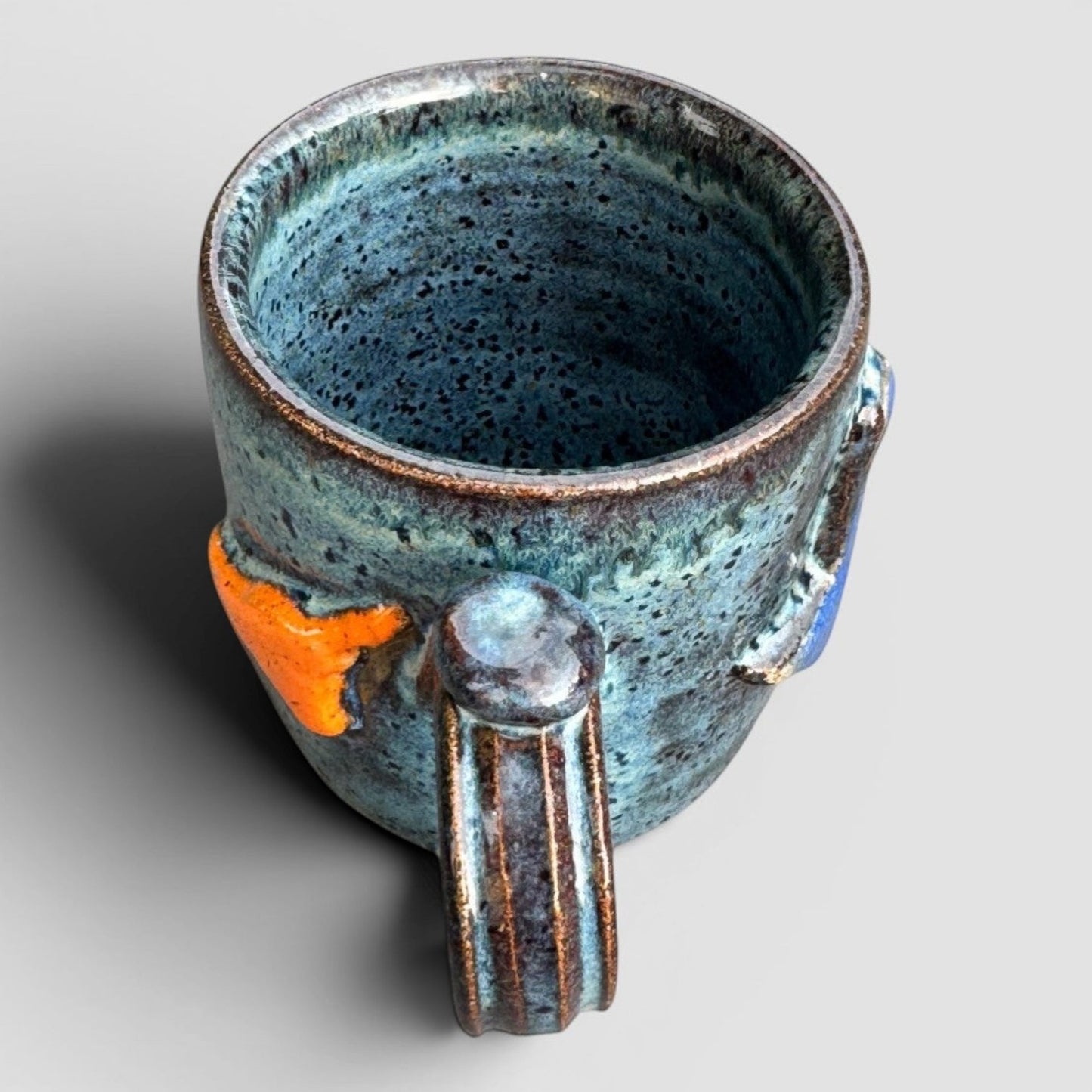 Rock N Art Shop handmade stoneware mug with speckled blue-green glaze and raised orange and blue state design.