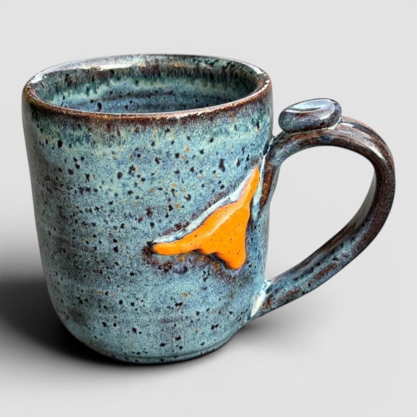 Rock N Art Shop handmade speckled blue stoneware mug with raised orange Texas shape. Holds 12 oz.