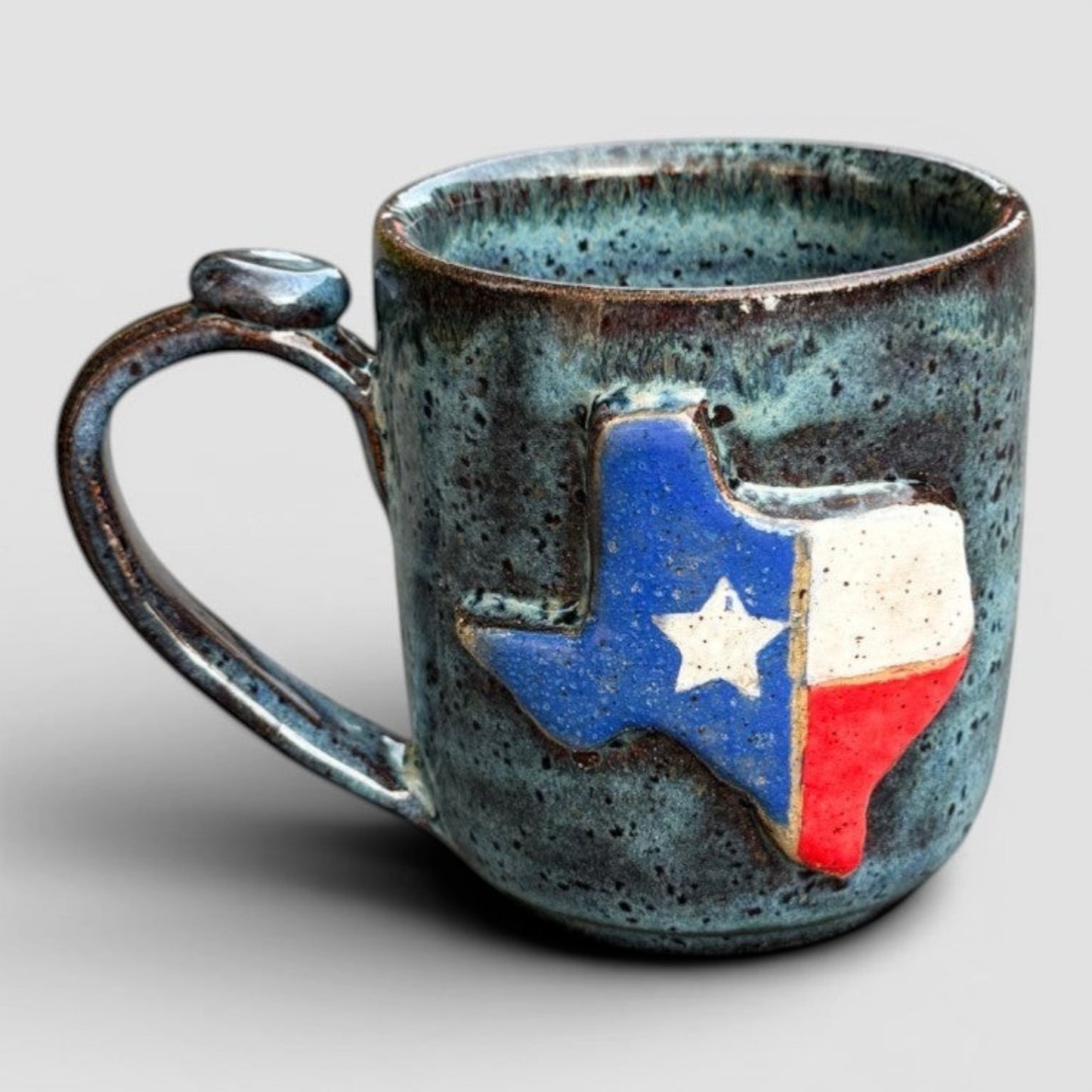 Rock N Art Shop handmade stoneware mug with Texas flag design, speckled blue-green glaze, 12 oz capacity.