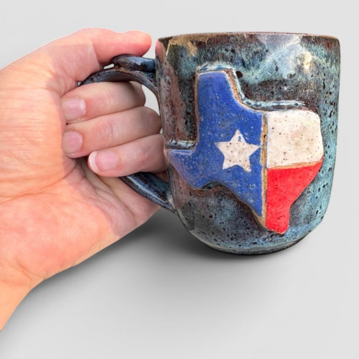 Rock N Art Shop handmade stoneware mug with a raised Texas flag design, speckled blue-green glaze.