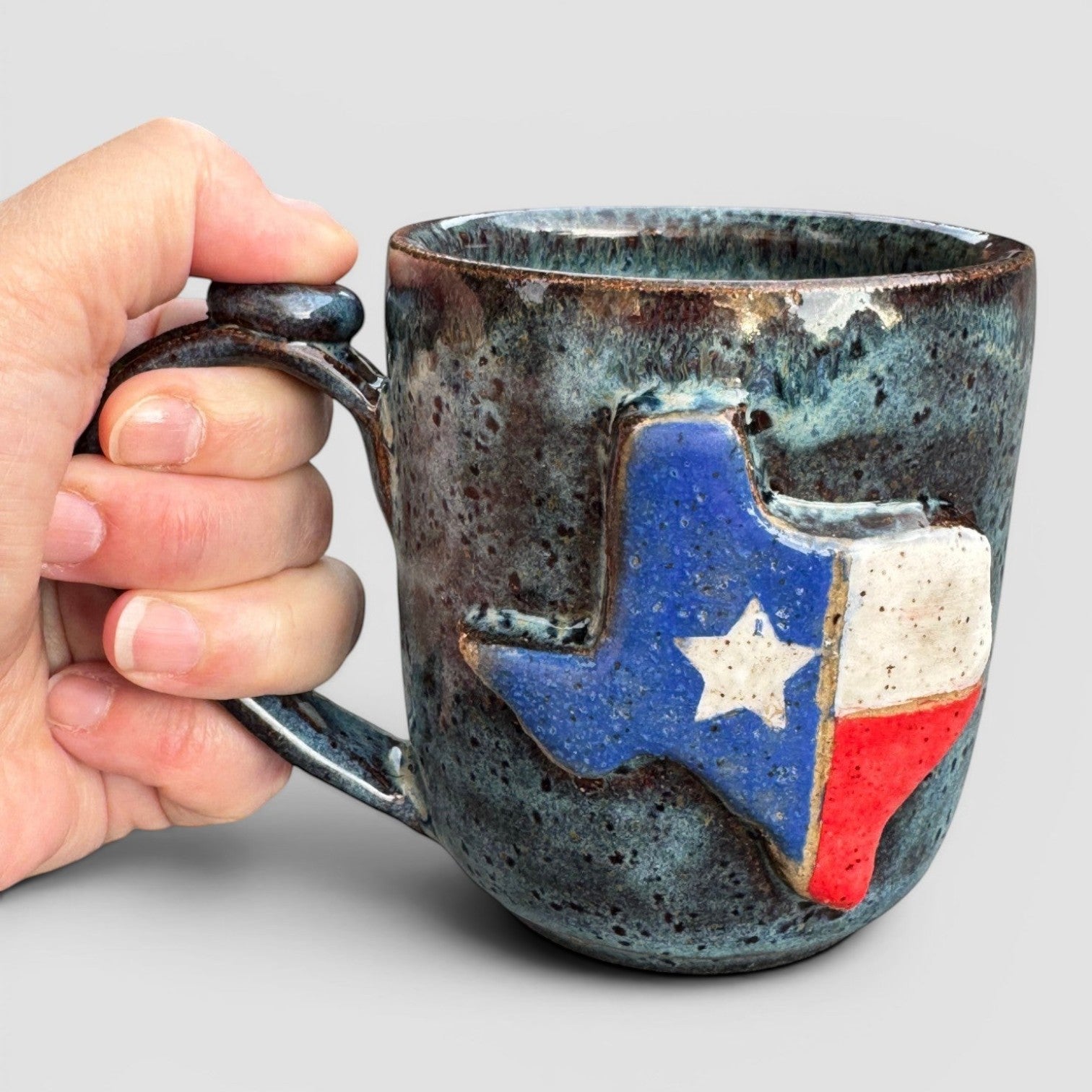 Rock N Art Shop handmade speckled blue stoneware coffee mug with a raised Texas flag design.