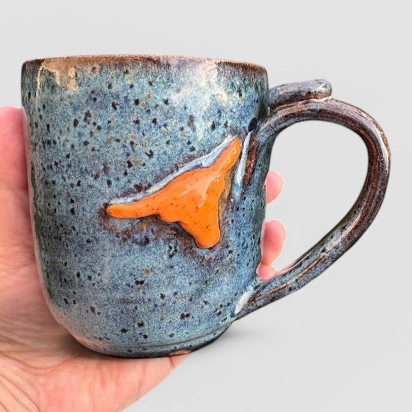Rock N Art Shop handmade speckled blue stoneware mug with raised orange Texas state design. Holds 12 oz.